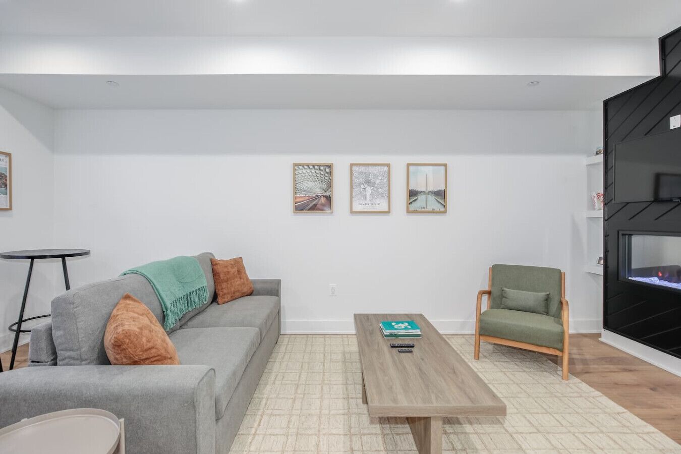 Un salon moderne avec un canapé gris, une table basse en bois, un fauteuil vert et une cheminée noire.