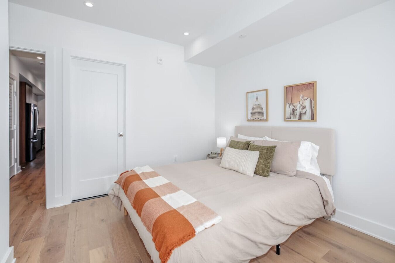 Un dormitorio con cama, mesita de noche, una puerta y un pasillo que conduce a una cocina.