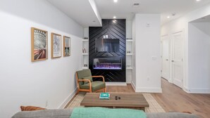 Un salon moderne avec une cheminée, un fauteuil vert, une table basse et des œuvres d’art encadrées accrochées au mur.