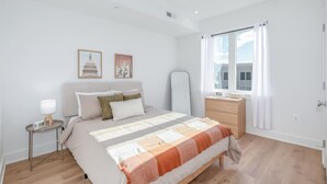 Une chambre à coucher avec un lit, une table de chevet, une lampe et une fenêtre avec des rideaux.