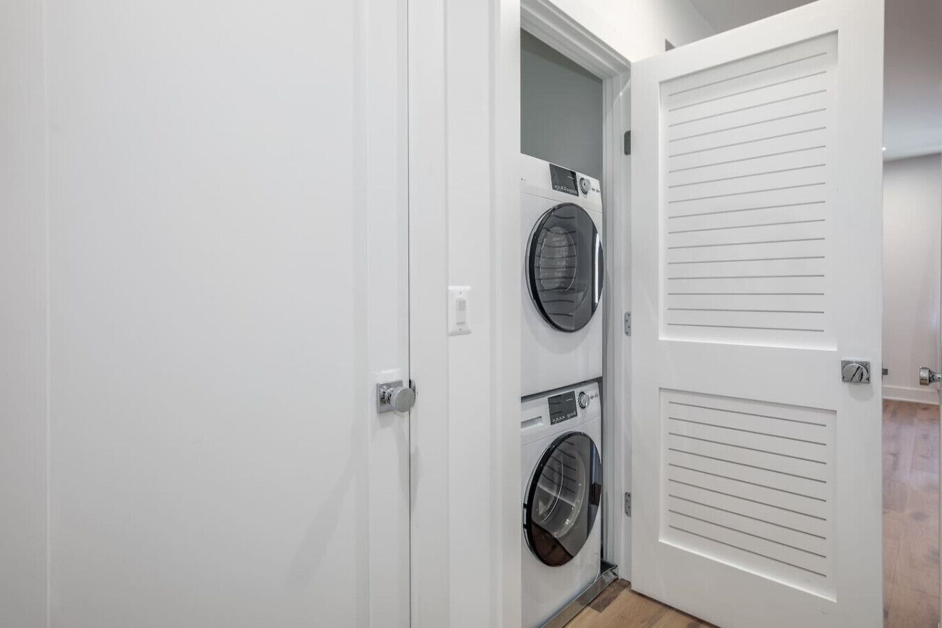 Une buanderie équipée de deux machines à laver et de deux sèche-linge à chargement frontal superposés, avec des portes blanches et un plancher en bois.