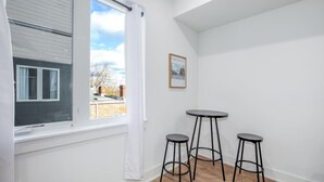 Une pièce avec une grande fenêtre, une petite table ronde et deux tabourets de bar.