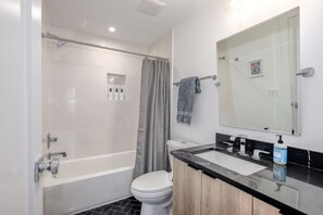 Un baño moderno con cabina de ducha de vidrio, inodoro blanco, tocador blanco y negro y un espejo grande.