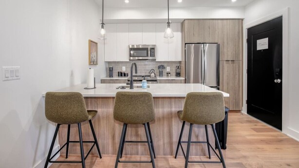 Une cuisine moderne dotée d’un îlot central, d’appareils électroménagers en acier inoxydable et de tabourets de bar.
