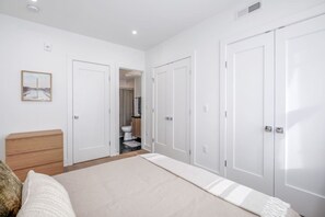 Un dormitorio con cama, cómoda de madera y puerta que da a un baño.