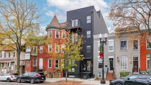 Une rangée d’immeubles à étages, présentant un mélange de styles architecturaux, notamment un bâtiment moderne de couleur noire et des bâtiments traditionnels en briques rouges.