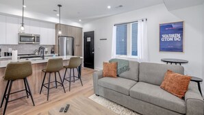 Un appartement moderne comprenant une cuisine, un coin repas et un salon. Il est équipé d’un canapé, de fauteuils et d’un téléviseur.