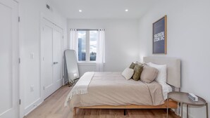 Une chambre à coucher avec un lit, une table de chevet, un miroir et une fenêtre avec des rideaux.