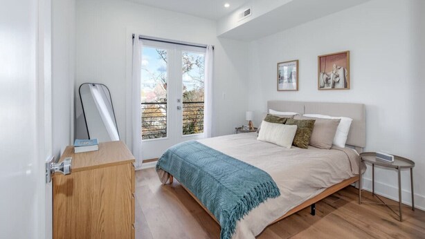 Une chambre à coucher comprenant un lit, une table de chevet, une commode, un miroir et une porte donnant sur un balcon.