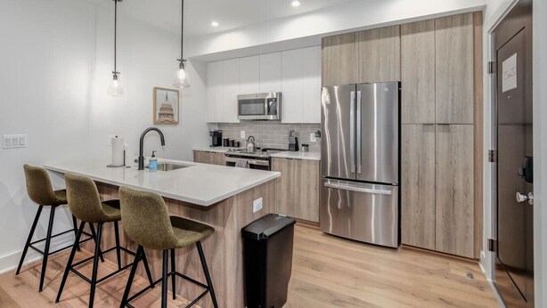 A modern kitchen with a central island, bar stools, stainless steel appliances, and wooden cabinetry.
