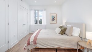 A bedroom with a bed, a bedside table, a window with curtains, and a framed picture on the wall.