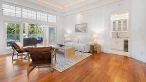 Un amplio salón con piso de madera, un sofá blanco, una mesa de centro y un comedor.