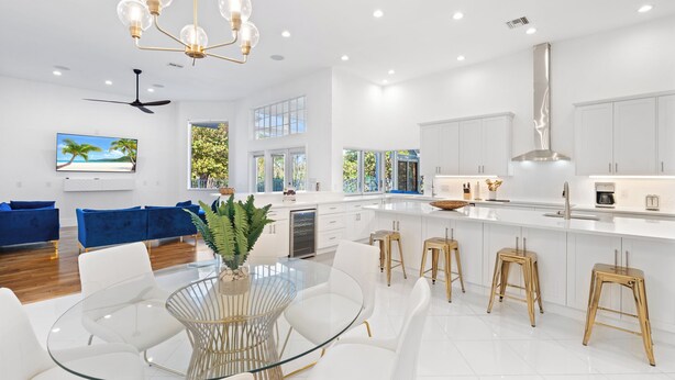 Una cocina moderna con armarios blancos, una isla central con taburetes y un amplio ventanal con vistas al verdor.