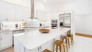 Una cocina moderna con armarios blancos, electrodomésticos de acero inoxidable y una isla central con taburetes.