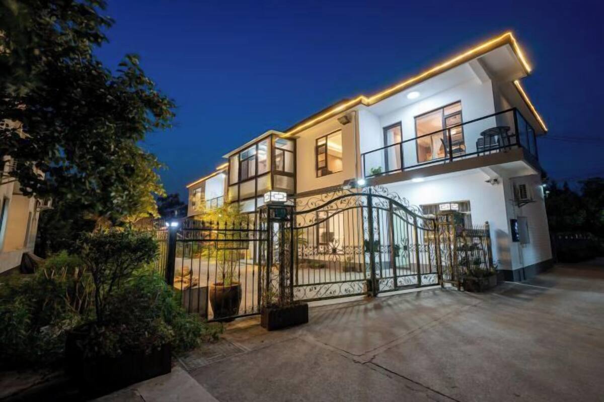 Une maison moderne à deux étages, dotée d’une entrée sécurisée par un portail, de grandes fenêtres et d’un balcon à l’étage supérieur.