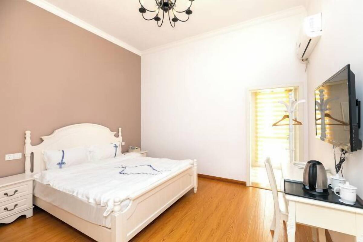 Une chambre avec un lit blanc, des tables de chevet, un bureau avec une bouilloire et une télévision.