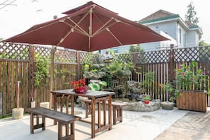 A patio with a wooden table and bench, a large umbrella, and a decorative rock garden. - Shanghai Dazaotou Homestay (Shanghai)
