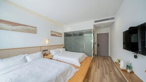 Habitación de hotel con dos camas, televisión, piso de madera y separador de vidrio.