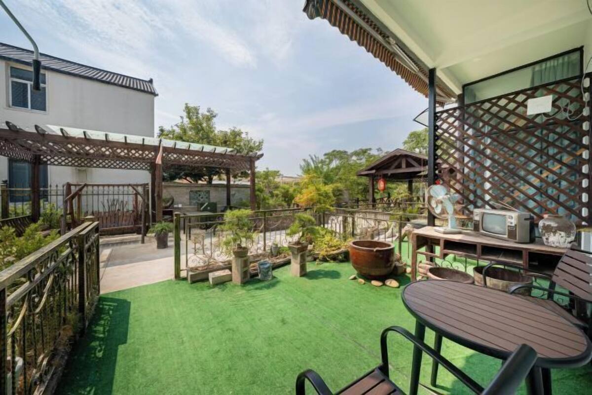 Une terrasse avec une pelouse artificielle verte, une table en bois avec des chaises et un téléviseur posé sur un meuble en bois.