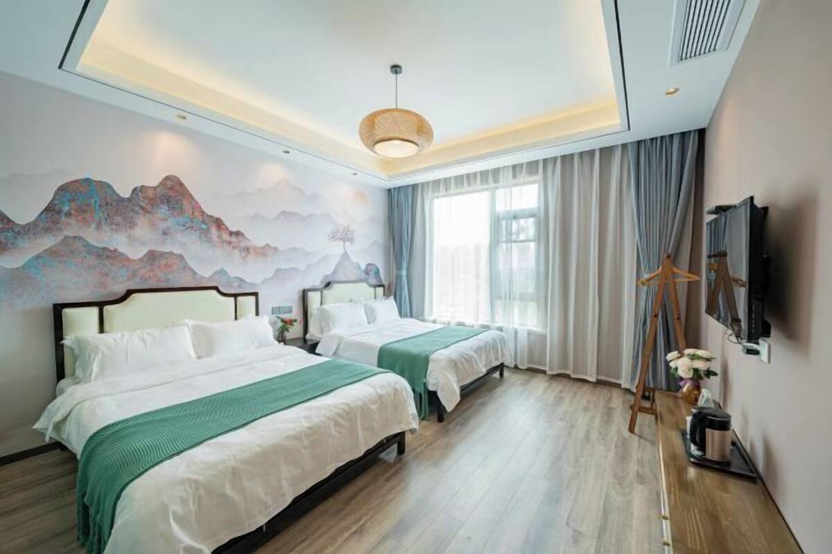 Une chambre d’hôtel avec deux lits, une grande fresque murale, un luminaire au plafond et une fenêtre avec des rideaux.