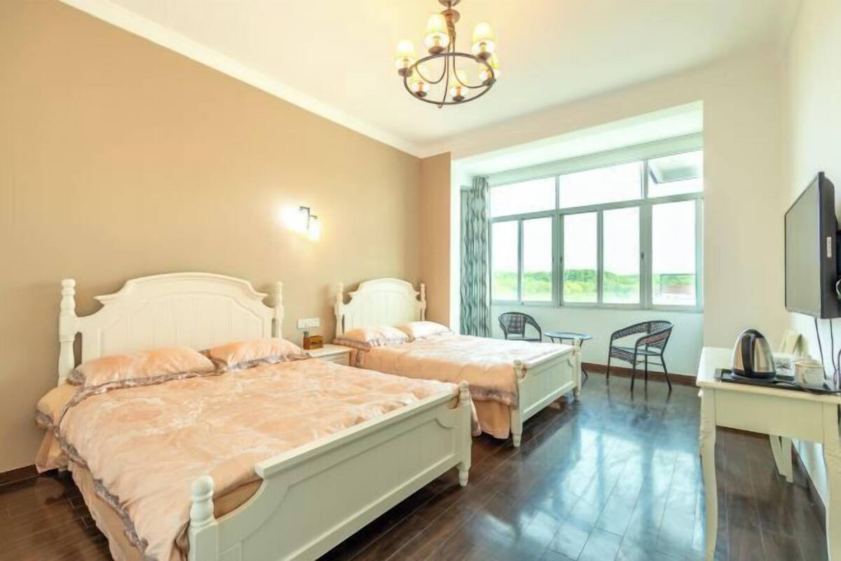 Une chambre avec deux lits, un bureau, une chaise, une télévision et une fenêtre donnant sur un beau paysage.