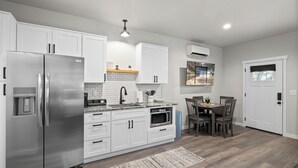 A modern kitchen with white cabinets, stainless steel appliances, a built-in oven, and a dining area with a table and chairs. - Bungalow 5 @ Barndo Bungalows (Granbury)