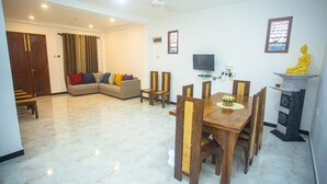 A living room with a sofa, a dining table with chairs, a television, and a statue.