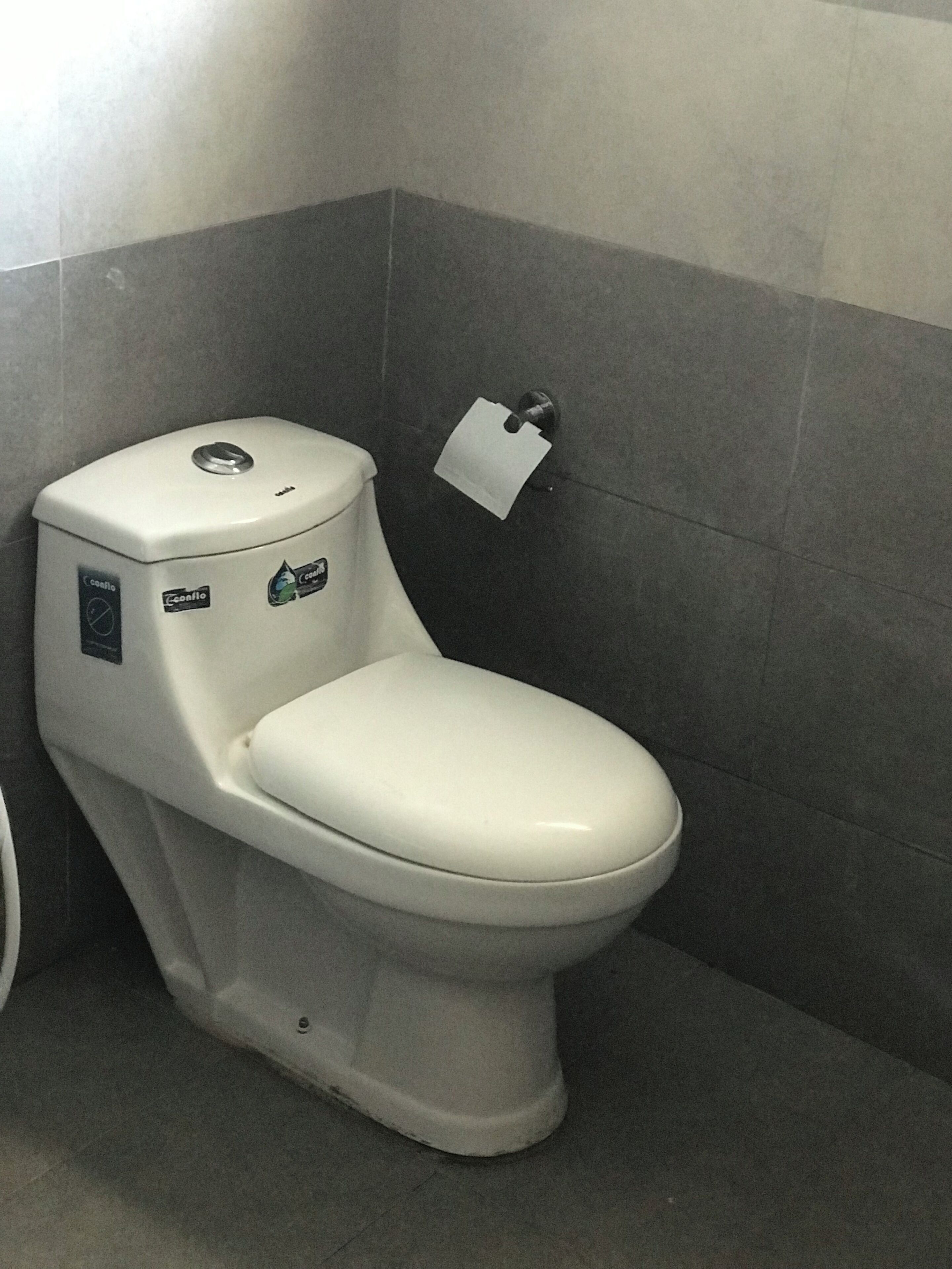 A white toilet with a control panel and a water-saving sticker in a bathroom with grey tiles.