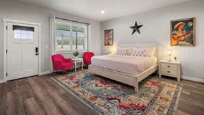 Une chambre à coucher comprenant un lit, une table de chevet, une chaise, une fenêtre avec des stores et une porte.