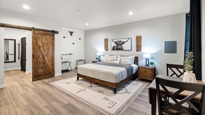 A modern bedroom with a large bed, wooden floor, and a sliding barn door. - Bungalow 4 @ Barndo Bungalows (Granbury)