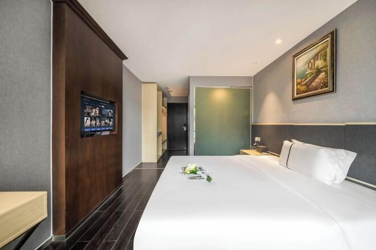 A hotel room with a large bed, a wooden panel wall, a framed picture, and a nightstand with a lamp.