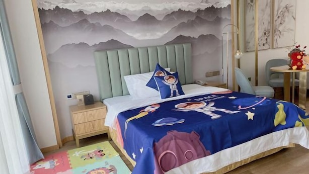 A bedroom with a bed covered in a space-themed bedspread, a nightstand, a desk, and a chair. - Bolianhui Hotel (Chongqing Southwest Hospital) (Chongqing)