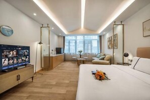 A modern hotel room with a large bed, a TV, a desk, and a sofa.