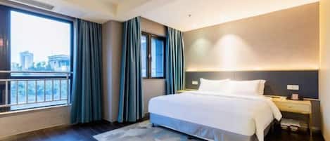 A modern hotel room with a large bed, a nightstand, a window with curtains, and a view of the city.