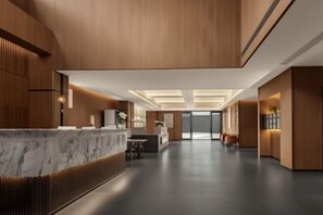 Un moderno hall de hotel con un mostrador de recepción de mármol, paneles de madera y un diseño espacioso.
