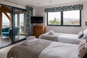 A bedroom with two beds, a TV, a wooden cabinet, and a view of the outdoors. - Sleeps 12, swimming pool, sea views, games rooms (Watermouth)