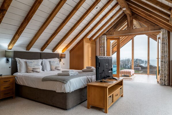 A bedroom with a large bed, wooden beams, a TV, and a view of the outdoors. - Sleeps 12, swimming pool, sea views, games rooms (Watermouth)