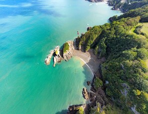 An aerial view of a coastal area with a beach, rocky outcrops, and dense greenery. - Sleeps 12, swimming pool, sea views, games rooms (Watermouth)