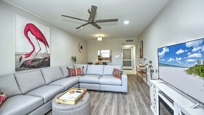 A modern living room with a grey sectional sofa, a ceiling fan, a flat-screen TV, and a wooden coffee table. - 5 min to Beach, Pool, Golf, BBQ! 1-bedroom penthouse w/elevator, WiFi, AC Naples (Naples)