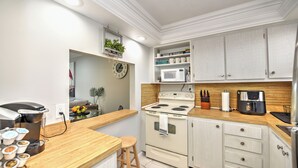 A modern kitchen with a wooden countertop, white cabinets, a microwave, a stove, and a coffee machine. - 5 min to Beach, Pool, Golf, BBQ! 1-bedroom penthouse w/elevator, WiFi, AC Naples (Naples)