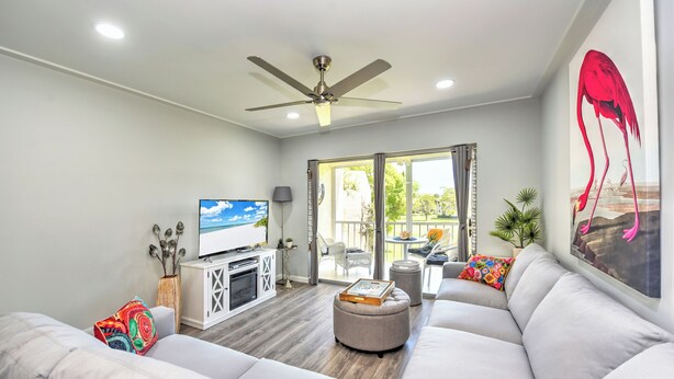 A modern living room with a white sofa, a ceiling fan, a TV, and a balcony with outdoor furniture. - 5 min to Beach, Pool, Golf, BBQ! 1-bedroom penthouse w/elevator, WiFi, AC Naples (Naples)