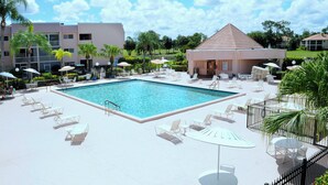 A swimming pool area with lounge chairs and umbrellas, surrounded by buildings and greenery. - 5 min to Beach, Pool, Golf, BBQ! 1-bedroom penthouse w/elevator, WiFi, AC Naples (Naples)