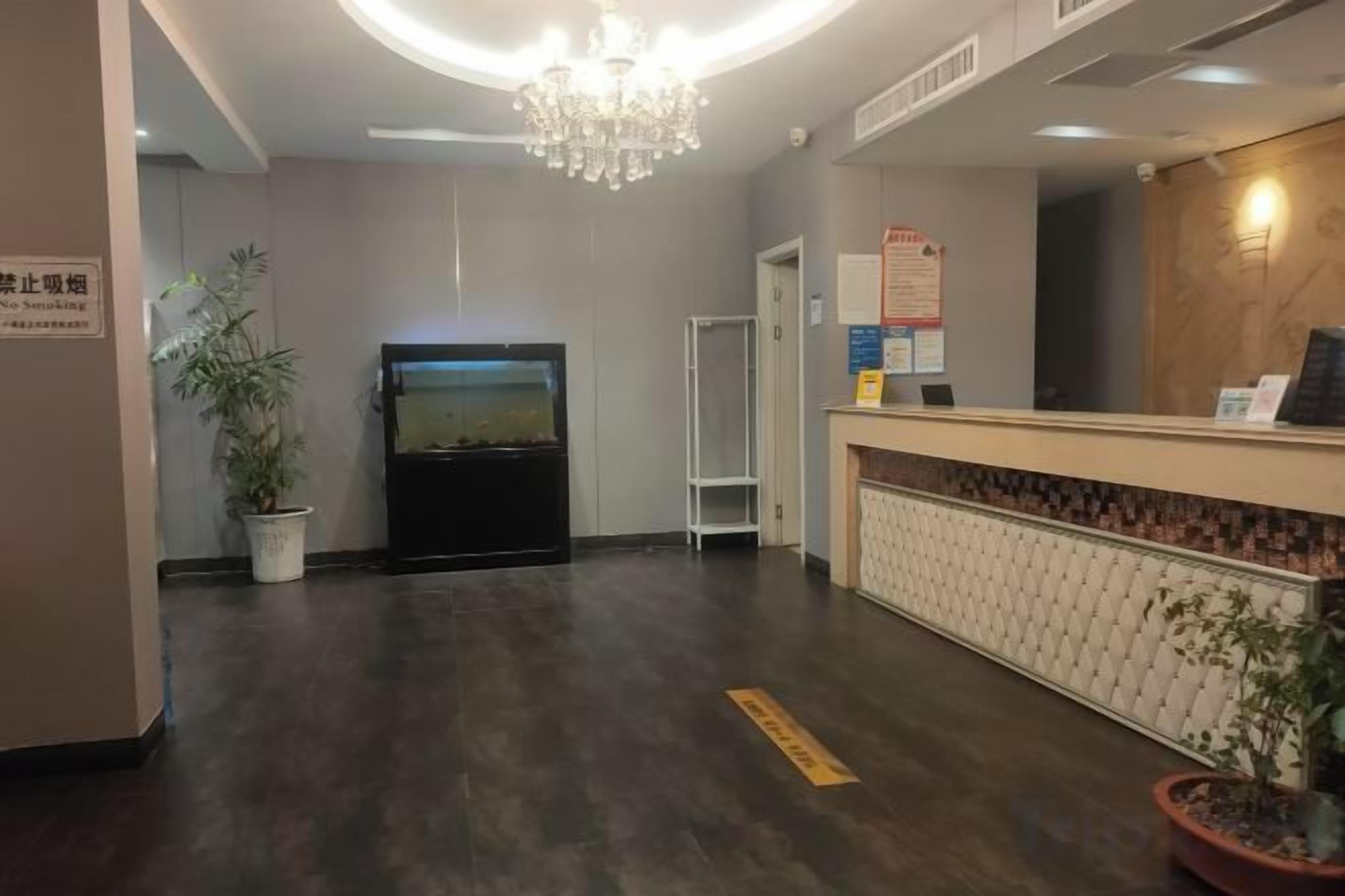Ein Hotel-Empfangsbereich mit Empfangstresen, einer Kronleuchter, einer Topfpflanze und einem wandmontierten Bildschirm.
