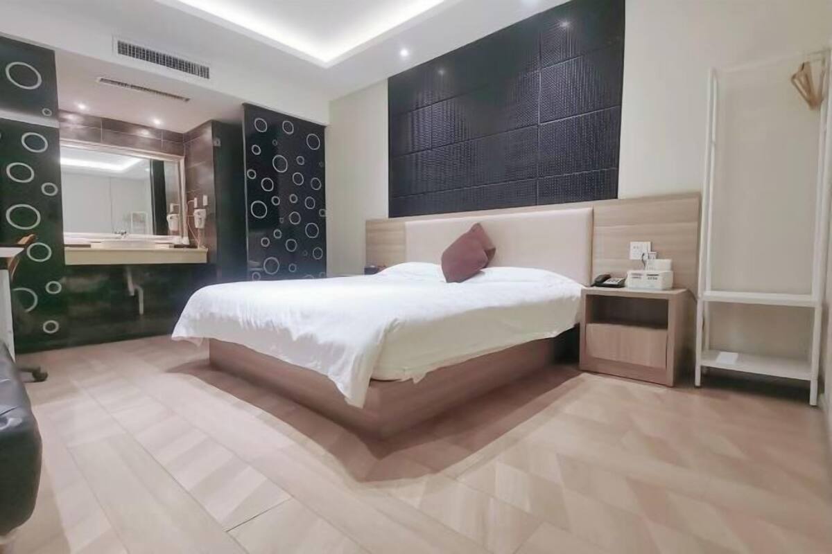 Una habitación de hotel moderna con una cama grande, una mesita de noche, un espejo y un panel fijado a la pared.