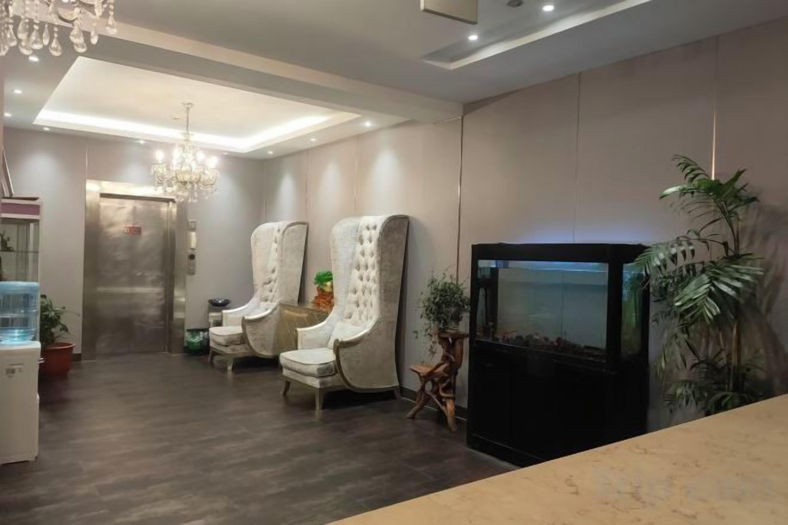 A modern interior with a reception desk, two upholstered chairs, a fish tank, and a television.