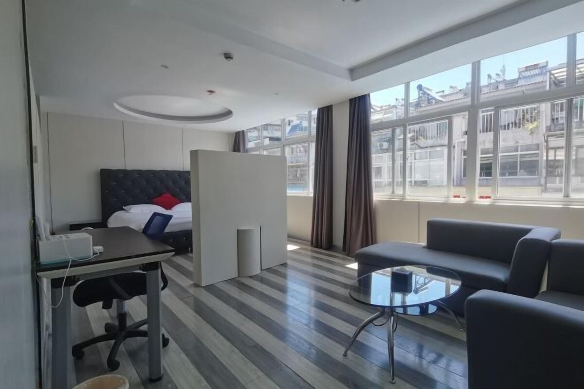 Una habitación de hotel con cama, escritorio, silla, sofá, una mesita y ventanas amplias.