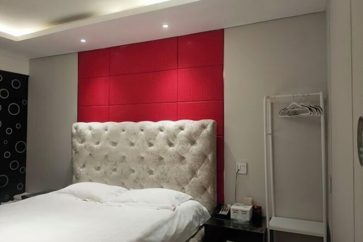 Quarto com cabeceira estofada, mesa de cabeceira com abajur e guarda-roupa com cabideiro.