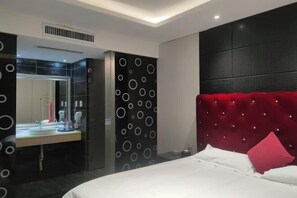 Un dormitorio moderno con una cama grande, un cabecero tapizado en rojo, una mesita de noche blanca y un espejo sobre el lavamanos.