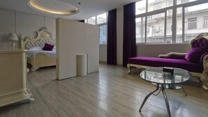 A hotel room with a bed, a sofa, a glass table, and a view of buildings through large windows. - Margarita Boutique Hotel (Guangde)