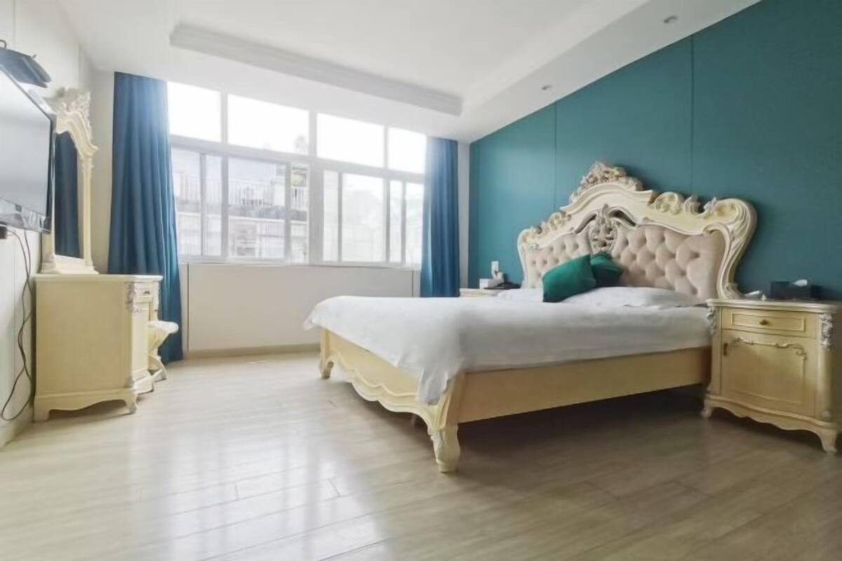 Un dormitorio con una cama grande, una mesita de noche, un aparador y una ventana con cortinas.